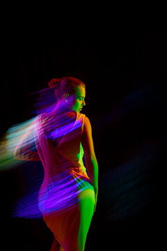 Back view of woman in white midi dress posing in neon light with long exposure against black mode background. Copy space for ad. Vertical image