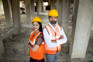 Portrait of two Indian male and female civil engineers or architect wearing helmet standing with cross arms. Real estate. Top angle