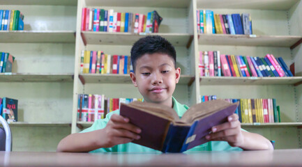 At the library, a young boy of Asian descent is deeply engrossed in reading a book during his break.