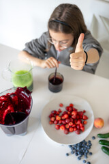 A teenage girl drinks a berry smoothie while sitting in the kitchen.