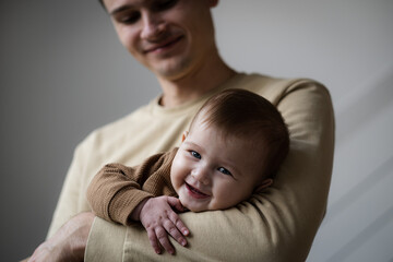 Man holding little five, six months baby smiling at home. Father and child indoors, Happy parenthood concept. Copy space.