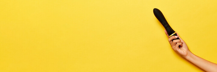 Banner. Female hand with vibrator, medical massager over yellow background. Image for sex shop. Concept of health, medicine, ad - obrazy, fototapety, plakaty