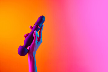Woman's hand holding vibrator, massager over yellow-pink background in neon light. Concept of toys...