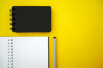 School notebook on a yellow background, black spiral notepad on a table.