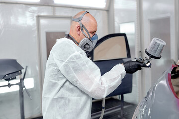 Man in overalls and a respirator expertly paints a car's parts inside a cutting-edge automotive...