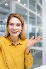 Vertical shot, female employee looking at phone camera waving and smiling, businesswoman talking...