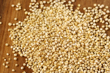 Raw quinoa kernels are heaped into a wooden spoon. Cereal seeds close-up. Macro