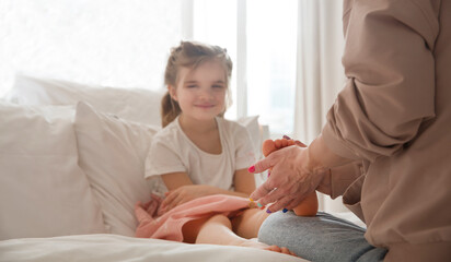 Mom massages her little daughter's feet with aroma essential oils sitting on the bed at home. Aroma...