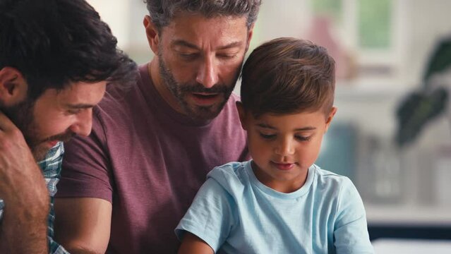 Close up of same sex family with two Dads in kitchen at home with son sitting at counter doing jigsaw puzzle together - shot in slow motion