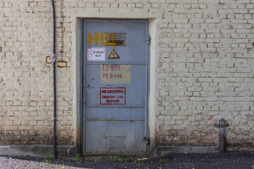 The door to the old brick electrical substation with warning signs in Russian: 