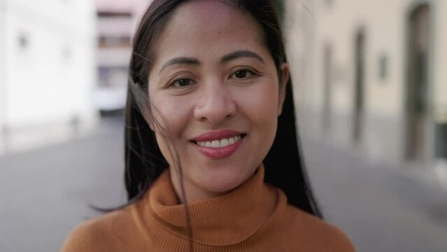 Happy Asian woman smiling on camera outdoor with city on background