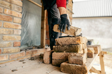 A builder is taking a brick from a pile on a building area.