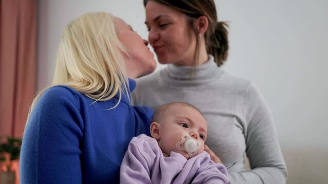 Happy gay lesbian couple and baby infant having tender moment at home - LGBTQ family and mothers love