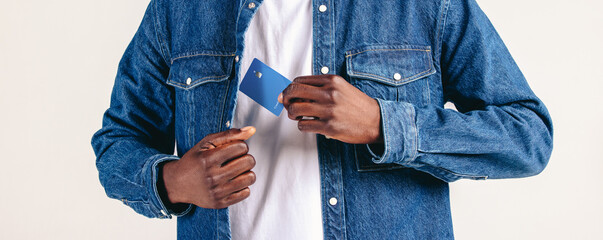Man in a denim jacket pulls a credit card from his pocket in a studio setting