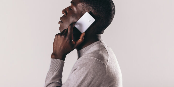 Making The Call To Premium Electronic Banking: Young Black Man Holds A Credit Card Over His Ear In A Studio