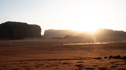 Sunset in front of vast Wadi Rum, Jordan with two jeeps driving across the desert creating dust...