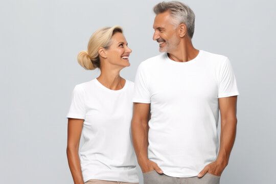 Elderly couple in matching white t-shirt mockup, happily posing on white studio backdrop.