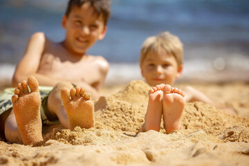 Child, tickling sibling on the beach on the feet with feather, kid cover in sand, smiling, laughing