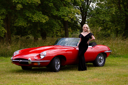 beautiful blond woman posing next to an immaculate red E-type Jaguar