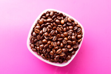 Top view of roasted coffee beans in bowl on pink background