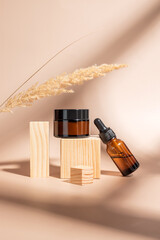 close up of collagen cream and beauty oil in glass jar and dry flowers reeds on beige background on wooden podiums. Set for skin and body care beauty products