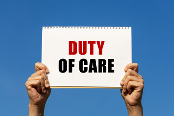 Duty of care text on notebook paper held by 2 hands with isolated blue sky background. This message can be used as business concept about duty of care.