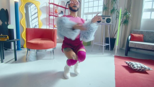 Crossed dressed lgbtq ballroom performer with beard and makeup wearing trendy dress dancing vogue and looking at camera in studio with creative interior. Zoom shot