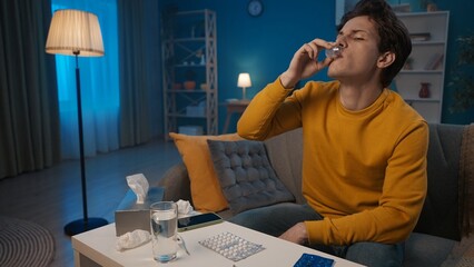 A sick man drinks cough syrup, antipyretic or anti-inflammatory. A man is sitting on the sofa in...