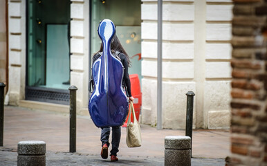 girl carries a cello in a blue trunk by the quiet European Street