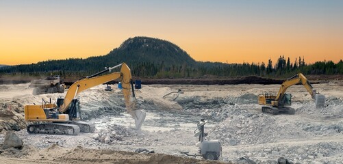 Excavators placing stones in an excavation at sunset with a mountain in the background