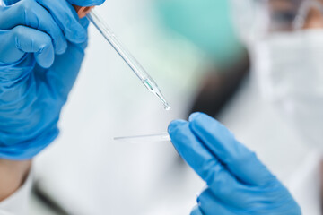 Scientist analyzing microscope slide at laboratory. Young woman technician is examining a histological sample, a biopsy in the laboratory of cancer research, Hand in blue glove holding glass histology