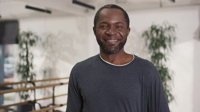 Portrait of African American man wearing sportswear and standing in modern fitness studio. Middle-aged male positively smiling while looking at camera. Having good feelings after hard training.