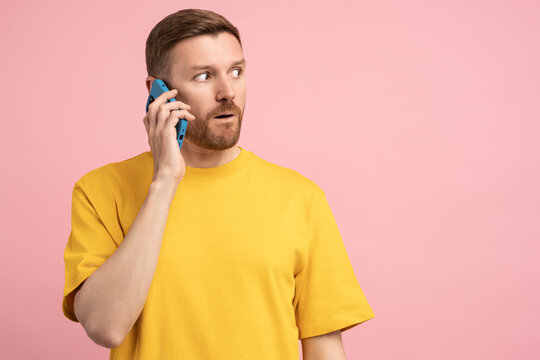 Amazement man looks away talking on mobile phone on pink background. Surprised guy have cellphone conversation with expression of emotions from promotional offer. Astonishment male by smartphone call