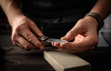 Man's hands with folding knife and sharpen stone tool. master sharpening penknife on a grindstone