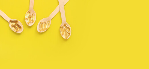 Omega 3. Gold capsules with fish oil in wooden spoons on a yellow background, top view....