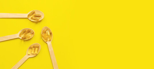 Omega 3. Gold capsules with fish oil in wooden spoons on a yellow background, top view....