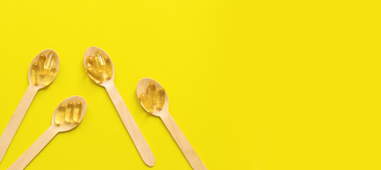 Omega 3. Gold capsules with fish oil in wooden spoons on a yellow background, top view....