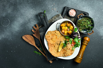 Large fried chicken schnitzel with vegetables. In a plate. On a black stone background. Photo of food.