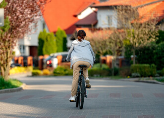 Cute laughing girl riding a bike in the evening in a calm city, back view. Eco-friendly urban transport.