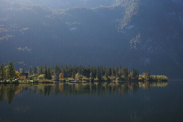 Fototapeta premium View of a mountain lake, a green shore with a forest and high mountains with morning sun rays