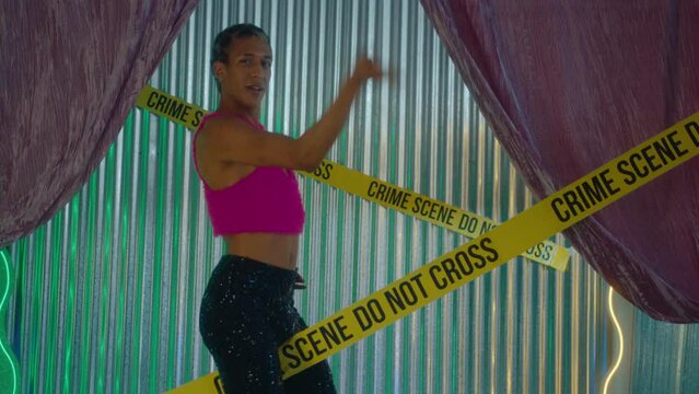 Feminine lgbtq ballroom performer with leopard print hair wearing stylish outfit posing and voguing on camera with yellow barricade tape between legs during photoshoot in studio