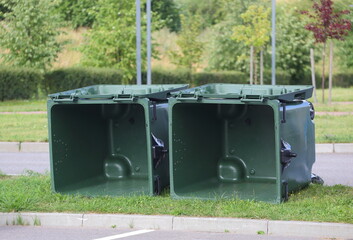 Two clean empty green plastic dumpsters are lying on the lawn