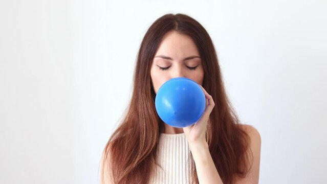 A beautiful woman inflates a blue balloon.