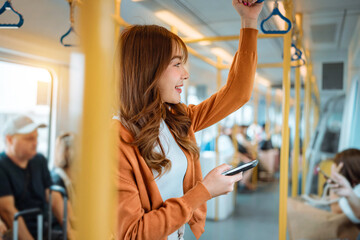 Happy young Asian woman passenger smile and using smart mobile phone in subway train station,...