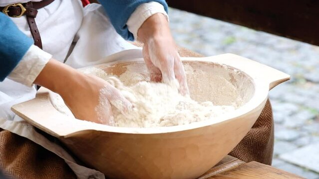 Woman dressed medieval costume sitting and kneading with hands fresh wheat dought. Healthy food and nutrition concept 4K footage