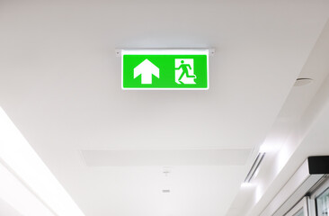 Lighted glowing green emergency exit signs in an office hallway with arrows pointing the way out of the building.