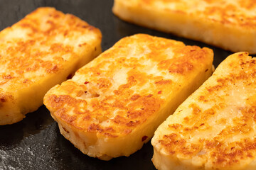 Detail of fried slices of halloumi cheese with red chilli on black frying pan.