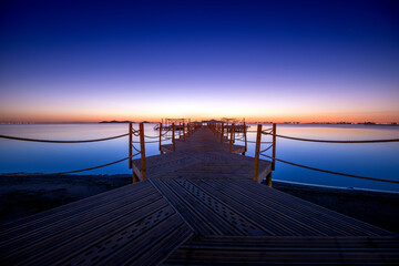 Fototapeta na wymiar Wooden jetty on Punta Brava beach in a warm sunrise, in Cartagena, Region of Murcia, Spain