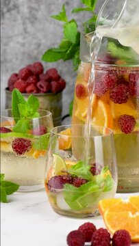 Filling a fruit glass with a Summer Sangria cocktail or lemonade with raspberry, orange and mint. Organic non-alcoholic, Detox, healthy drink The camera moves forward, slow motion. Vertical video 