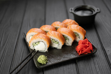 Sushi roll Philadelphia with salmon, cucumber and cream cheese served on plate with soy sauce and wasabi on black background. Sushi menu. Japanese food.